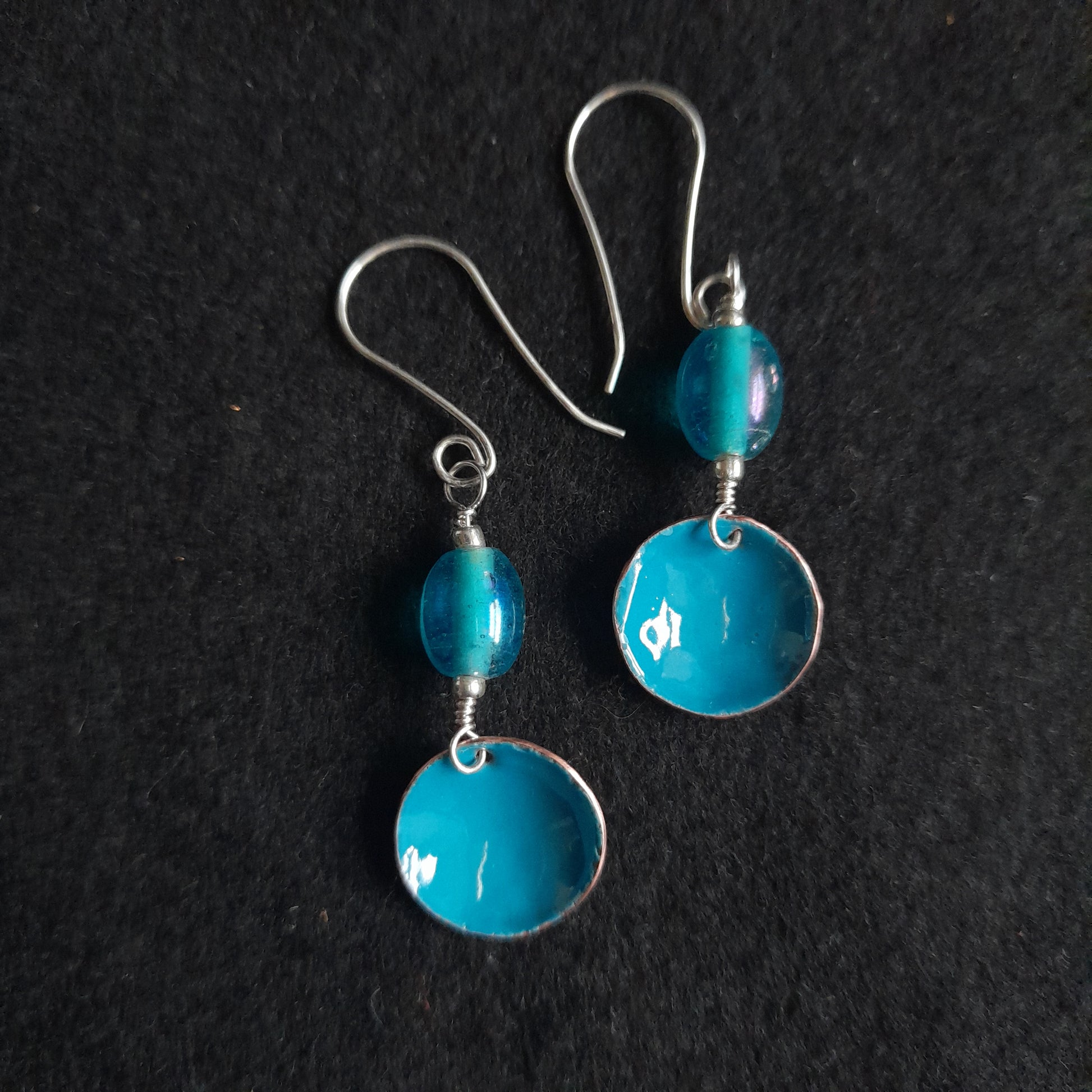 A pair of handmade blue enamel bowl dangle earrings, presented with a blue oval glass bead, set on silver earwires.