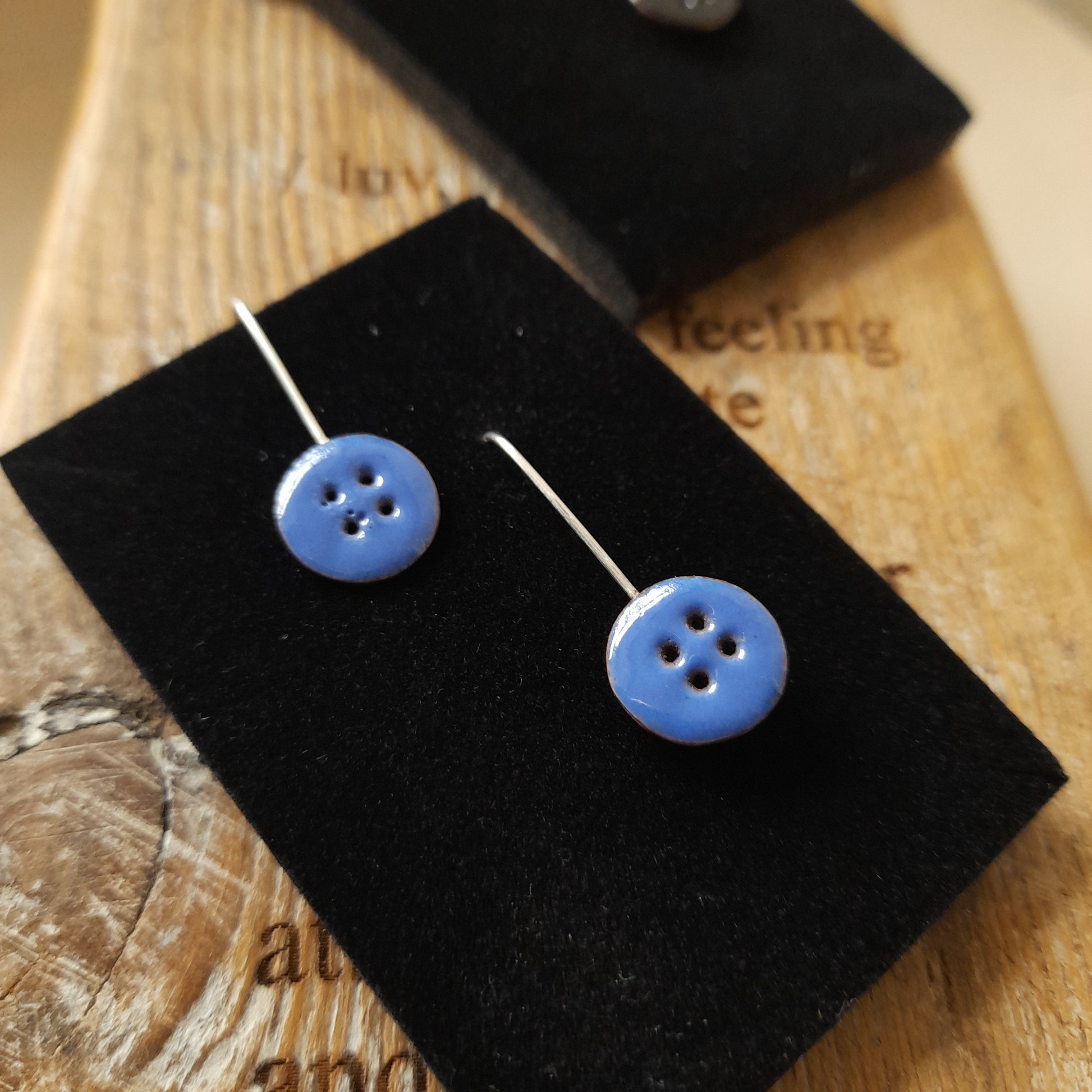 Quirky handmade button drop earrings, in blue with 4 holes. Displayed on a wood background.