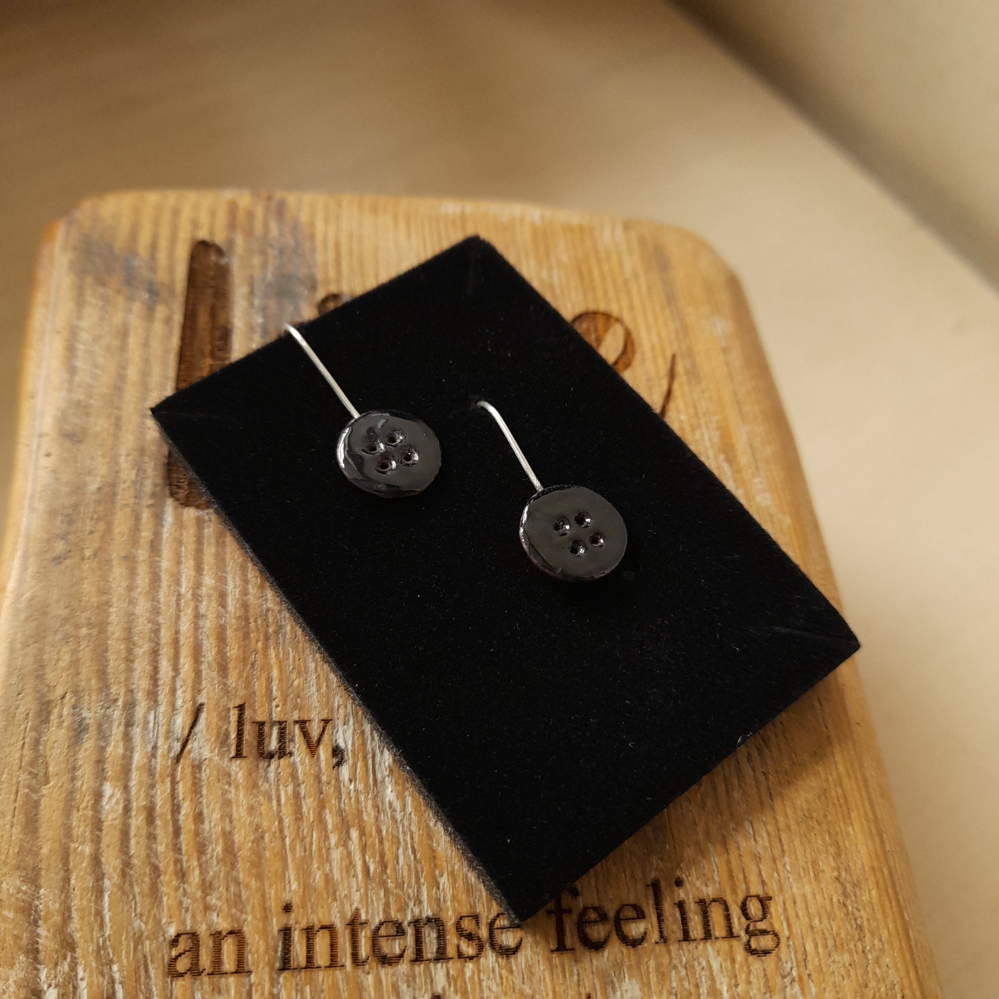 Quirky handmade button drop earrings, in black with 4 holes. Displayed on a wood background.