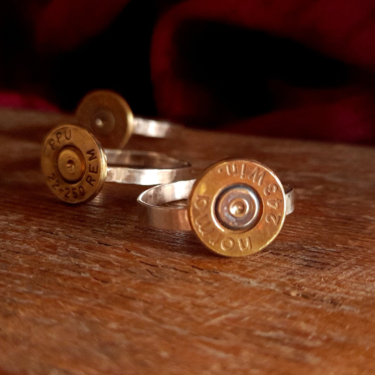 This image shows 3 cartridge rings in close up. They are on silver bands with the bottom of the cartridge soldered on like a signet ring, there is writing on the cartridge ends. They are on a grainy wood background