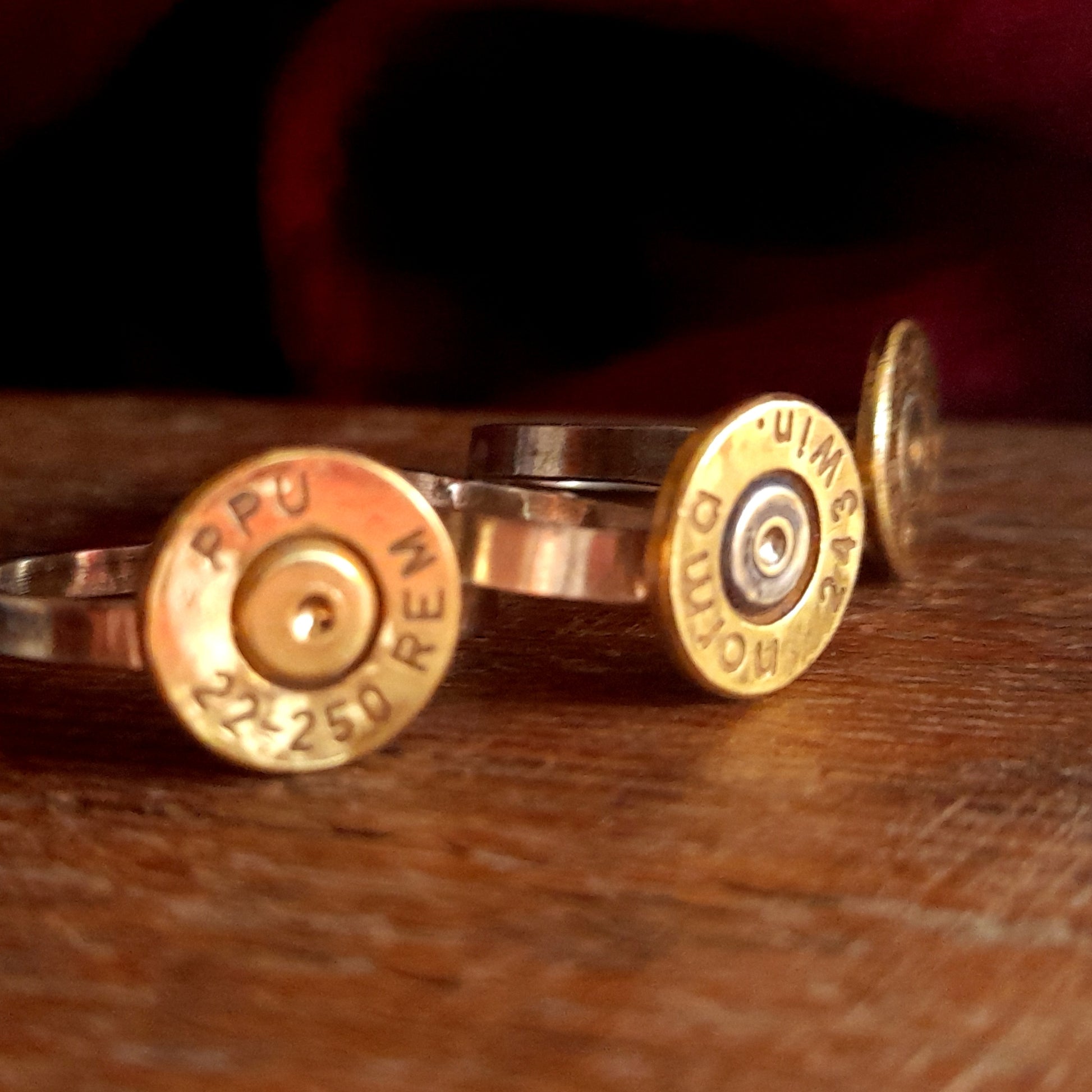 This image shows 3 cartridge rings in close up. They have copper bands with the bottom of the cartridge soldered on like a signet ring, there is writing on the cartridge ends. they are on a grainy wood background