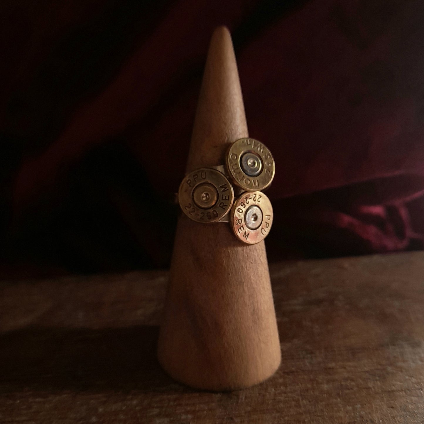 This image shows 3 cartridge ring in close up. They have silver bands with the bottom of the cartridge soldered on like a signet ring, there is writing on the cartridge ends. They are on a grainy wood background.