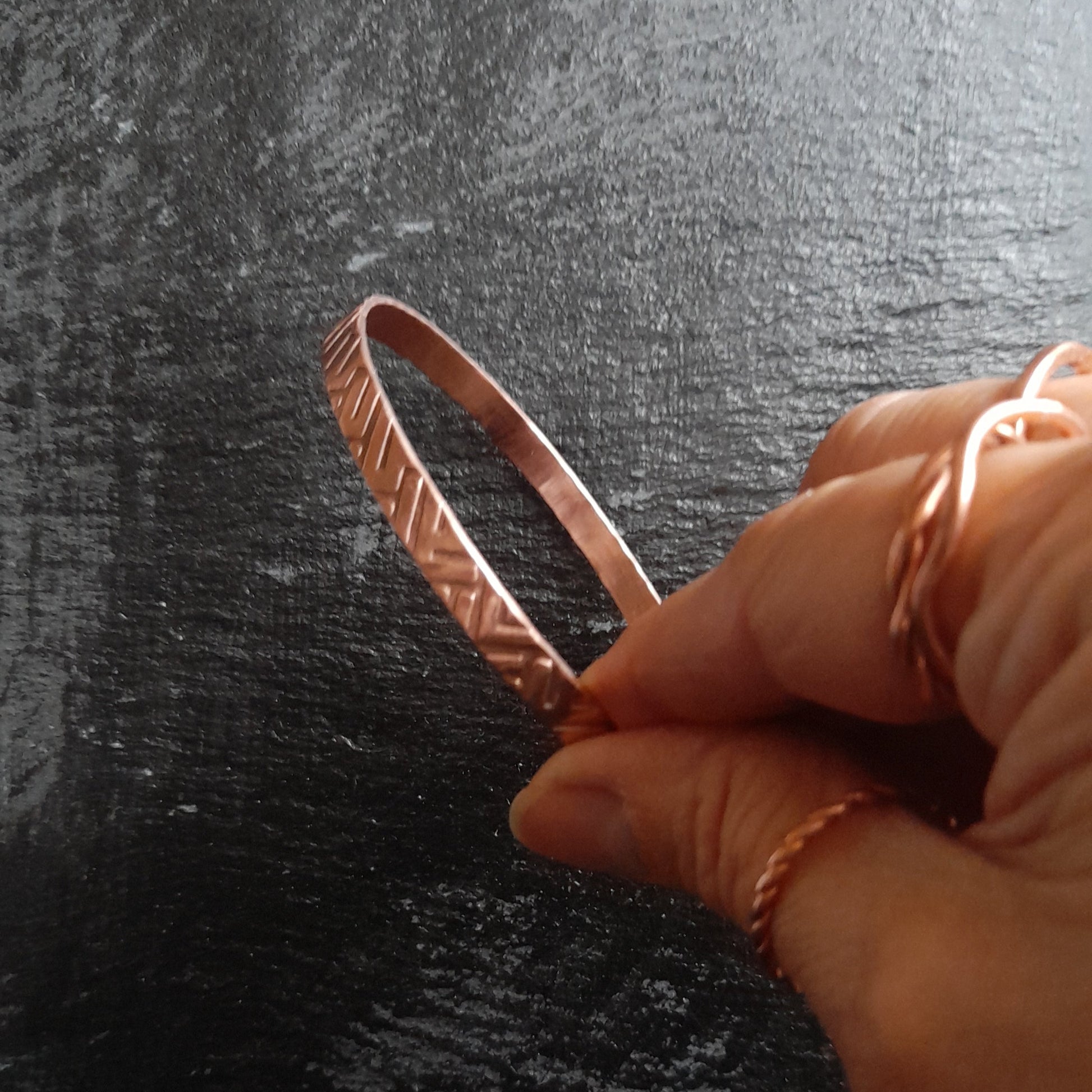 Copper bangle held in the fingers of a woman wearing copper rings 