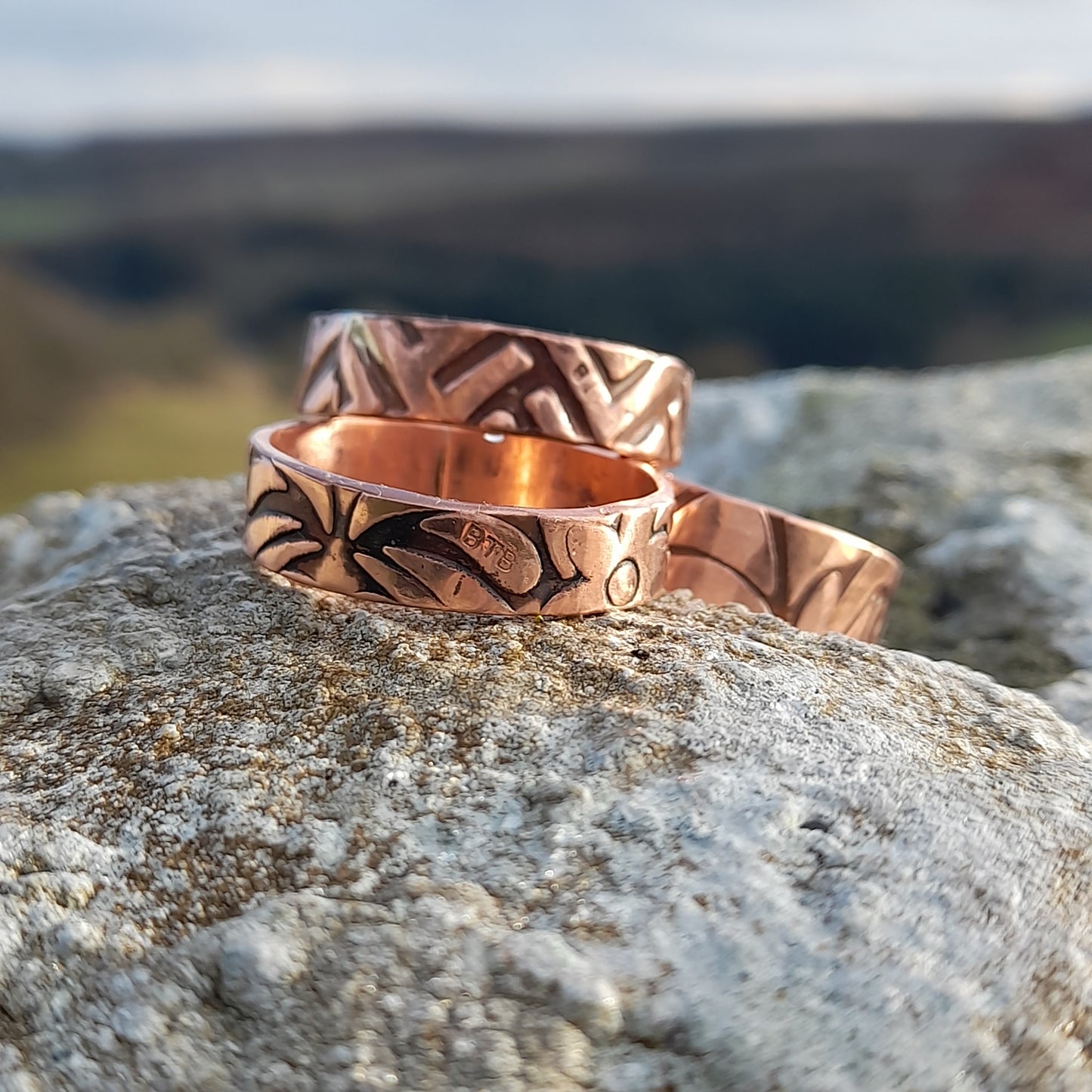 3 Patterned chunky copper rings on a white rock with hills in the background