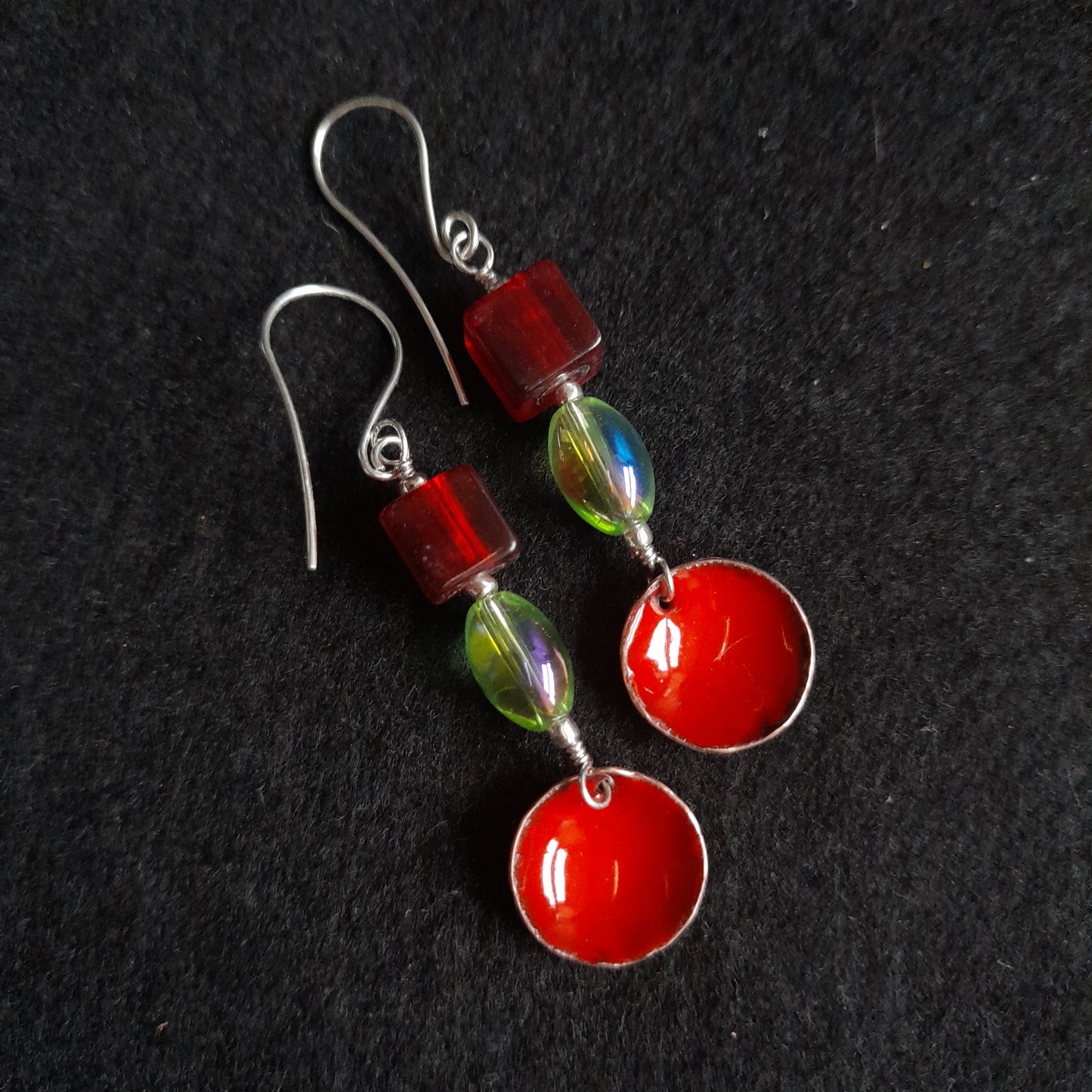 A pair of handmade red enamel bowl dangle earrings, presented with a red square and green oval glass bead, dangle earrings on silver earwires.