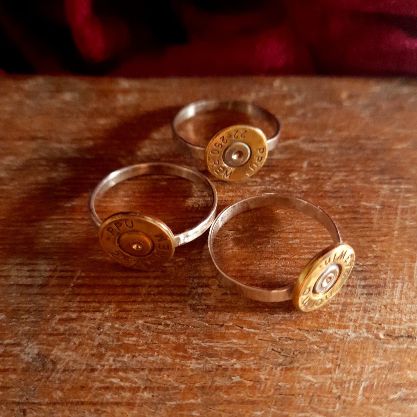 This image shows 3 cartridge rings in close up. They have copper bands with the bottom of the cartridge soldered on like a signet ring, there is writing on the cartridge ends. they are on a grainy wood background