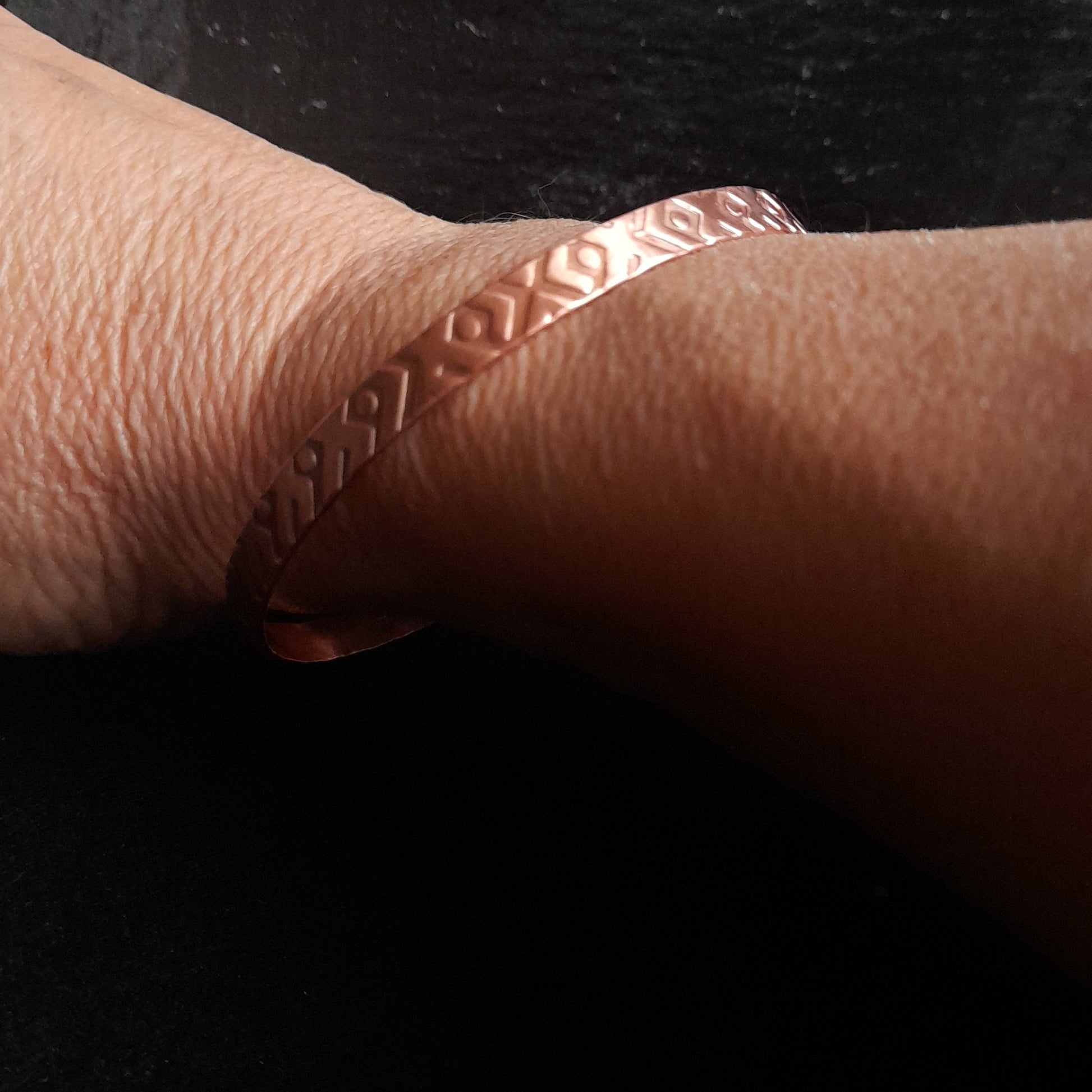 Copper bangle with geometric pattern displayed on a woman's wrist