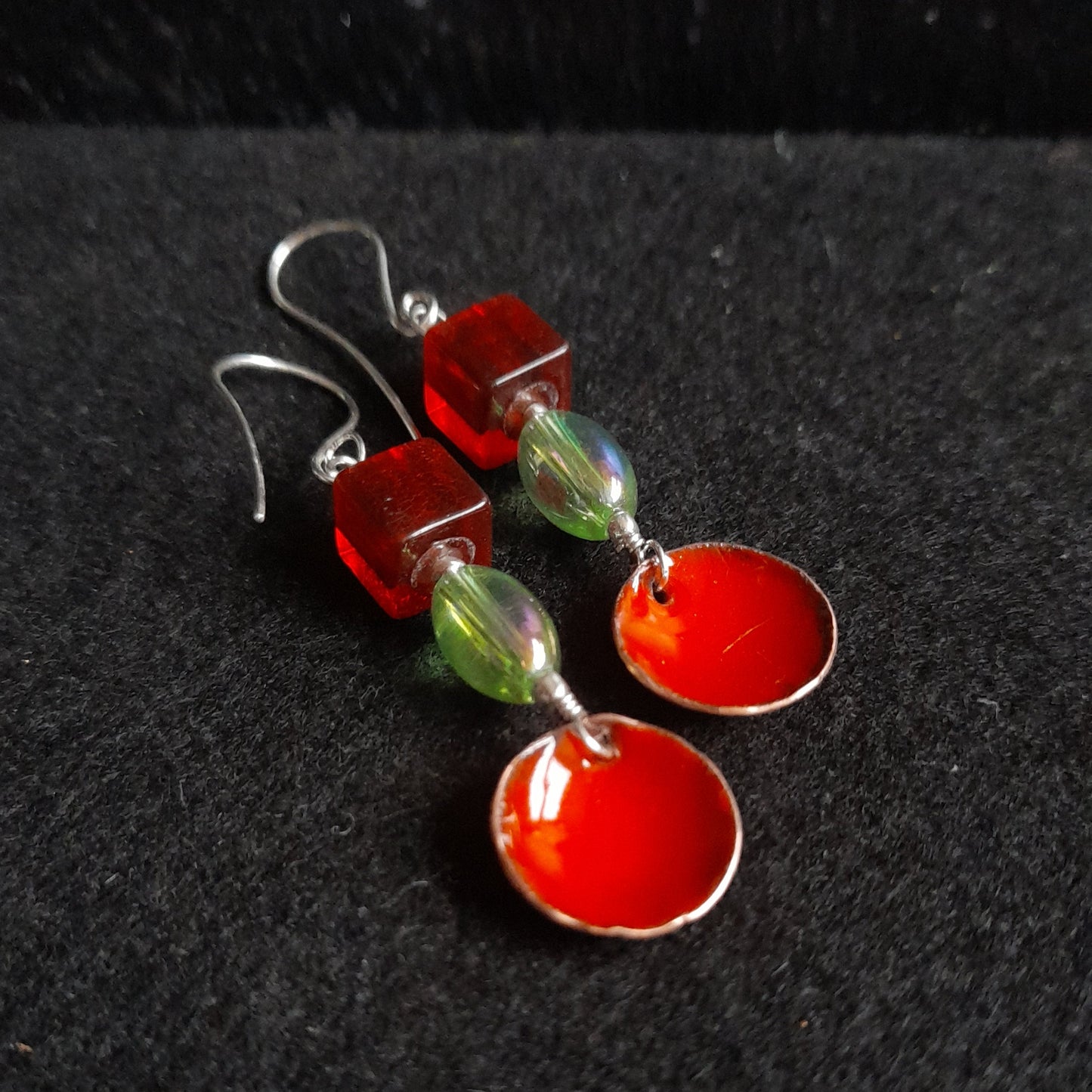 A pair of handmade red enamel bowl dangle earrings, presented with a red square and green oval glass bead, dangle earrings on silver earwires.