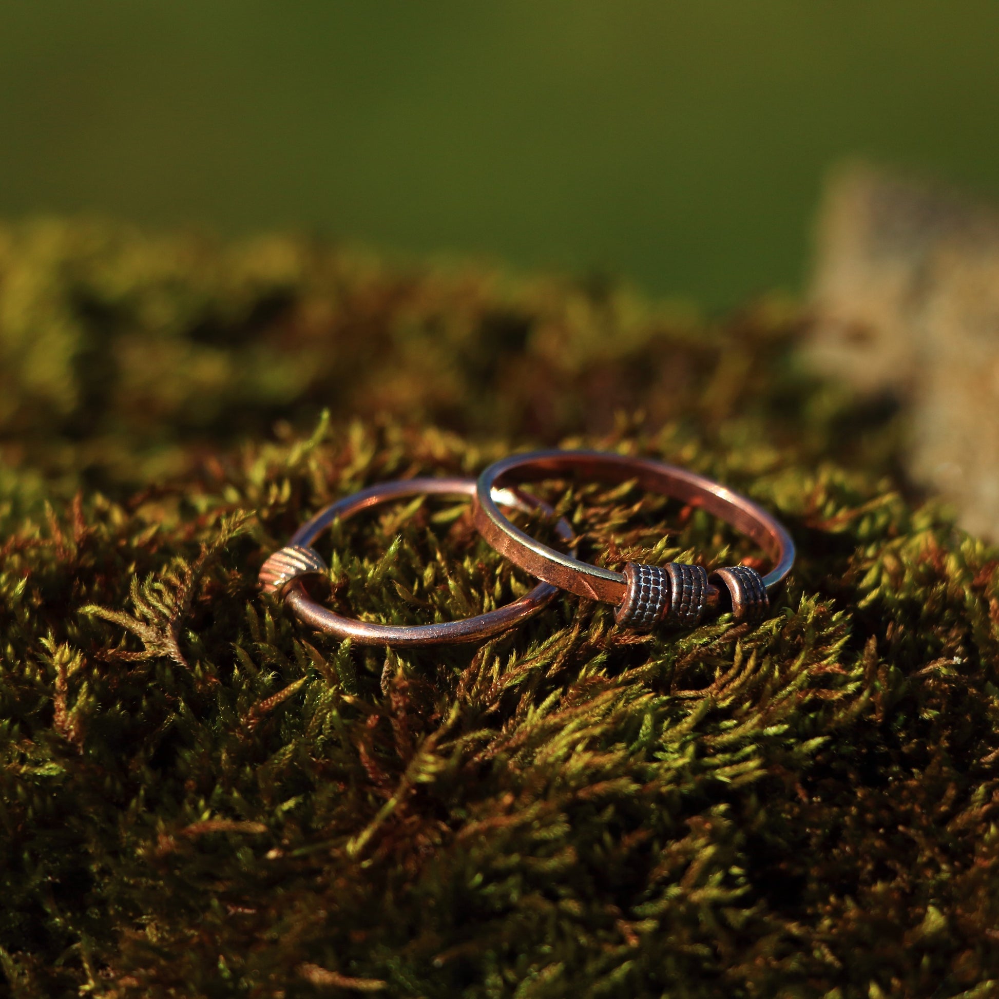 Two copper fidget rings, on round and flat wire, one has a brass textured cylinder bead  the other has three matching lightly silver textured cylinder beads.