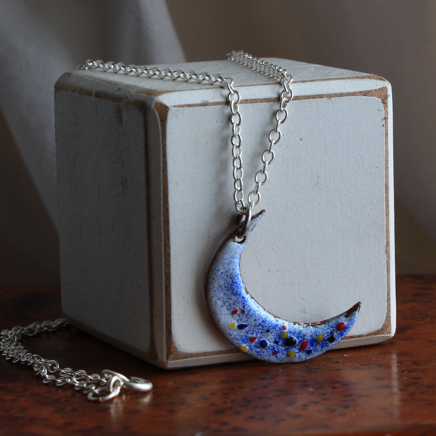 Crescent moon necklace in blue and white enamel, with multi-coloured flecks. On sterling silver chain, approximately 3cm long